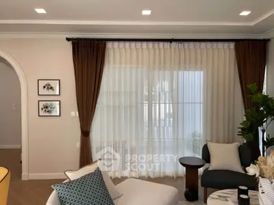 Elegant living room with stylish decor and large window draped with sheer curtains, creating a cozy ambiance.
