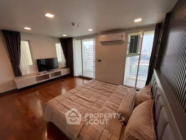 Spacious bedroom with balcony and city view, featuring modern decor and ample natural light.