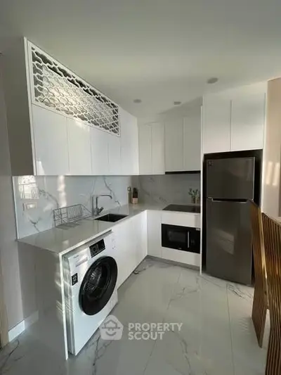 Modern kitchen with sleek white cabinets and built-in appliances, featuring a washing machine and elegant marble flooring.
