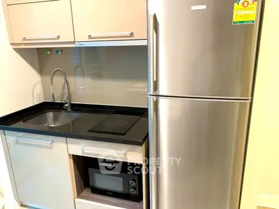 Modern kitchen with sleek appliances and compact design, featuring a stainless steel fridge and built-in microwave.