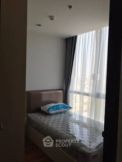Cozy bedroom with large window and modern decor in a high-rise apartment.