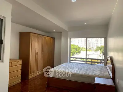 Spacious bedroom with large window and wooden furniture in modern apartment