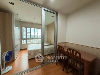 Cozy bedroom with wooden flooring and city view, featuring a study desk and sliding glass doors.