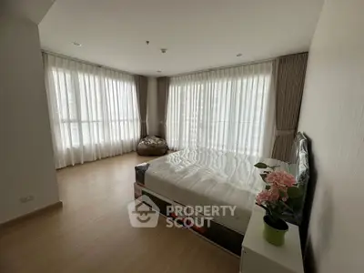 Spacious bedroom with large windows and natural light, featuring modern decor and a cozy atmosphere.