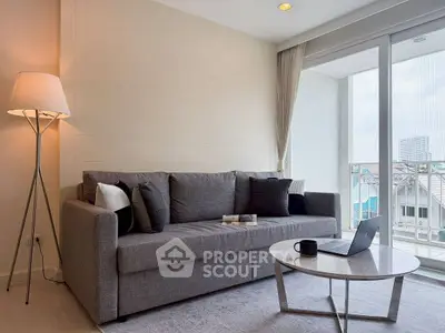 Modern living room with gray sofa and laptop on coffee table, bright natural light from large window.