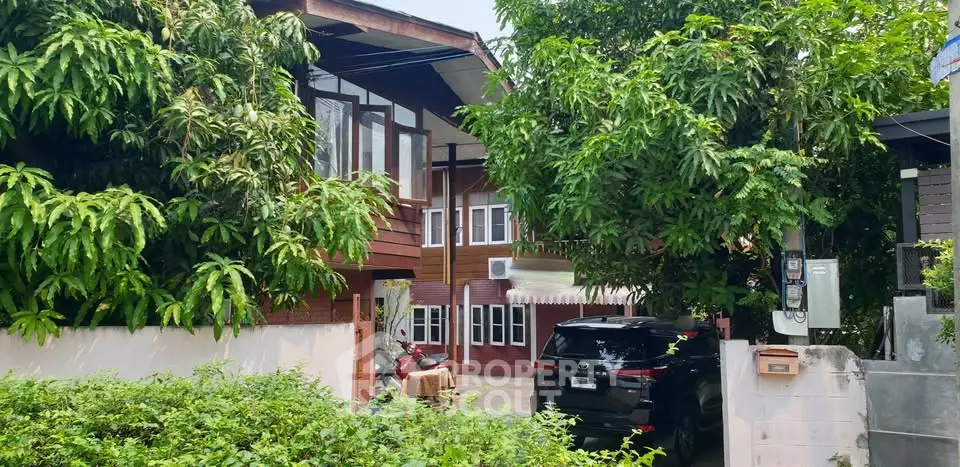 Charming traditional wooden house with lush greenery and modern SUV parked in driveway.