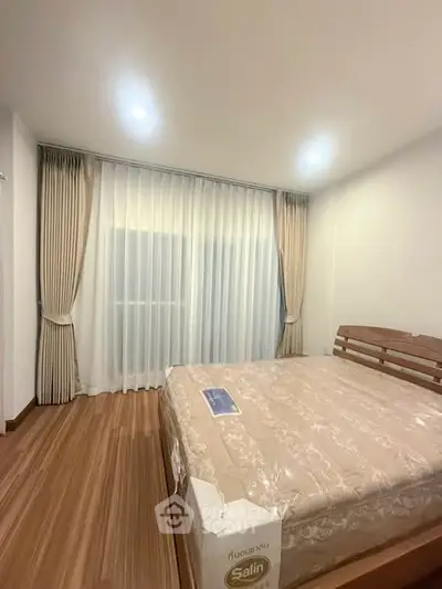 Spacious bedroom with elegant wooden flooring and large window with curtains, perfect for relaxation.