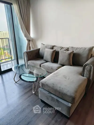 Modern living room with stylish gray sofa and glass coffee table, featuring a balcony view.