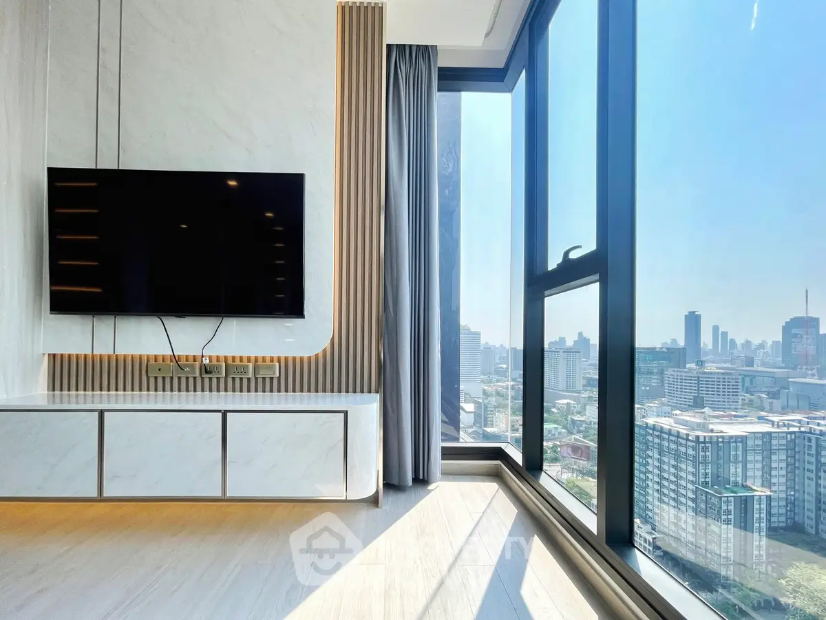 Modern living room with large windows offering stunning city views and sleek TV setup.