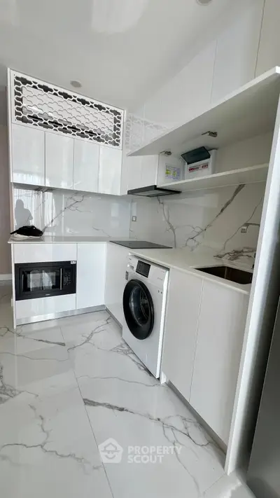 Modern kitchen with sleek white cabinetry and marble flooring, featuring built-in appliances and a washing machine.