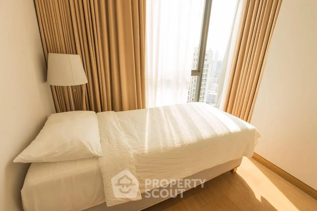 Bright and cozy bedroom with city view, featuring a single bed and elegant curtains.