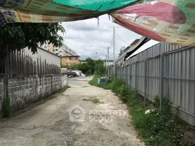 Narrow alleyway between residential buildings with overhanging tarp and cloudy sky.
