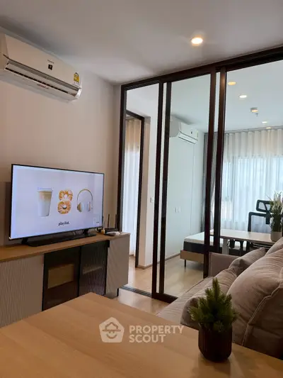 Modern living room with sleek design and glass partition, featuring a cozy sofa and large TV.