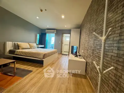 Modern bedroom with stylish brick accent wall and cozy wooden flooring, featuring a comfortable bed and sleek furniture.