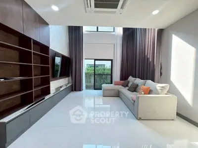 Spacious modern living room with high ceilings and large windows, featuring a cozy sectional sofa and sleek built-in shelving.