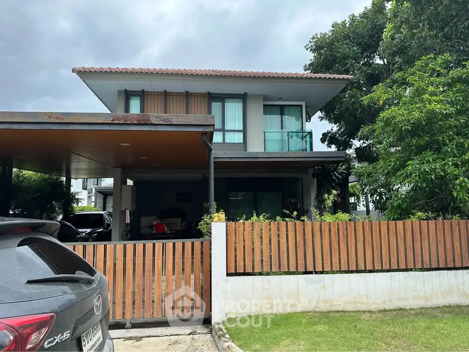 Modern two-story house with wooden fence and carport in lush green setting.