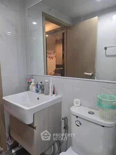 Modern bathroom with sleek sink and toilet, featuring a large mirror and minimalistic design.