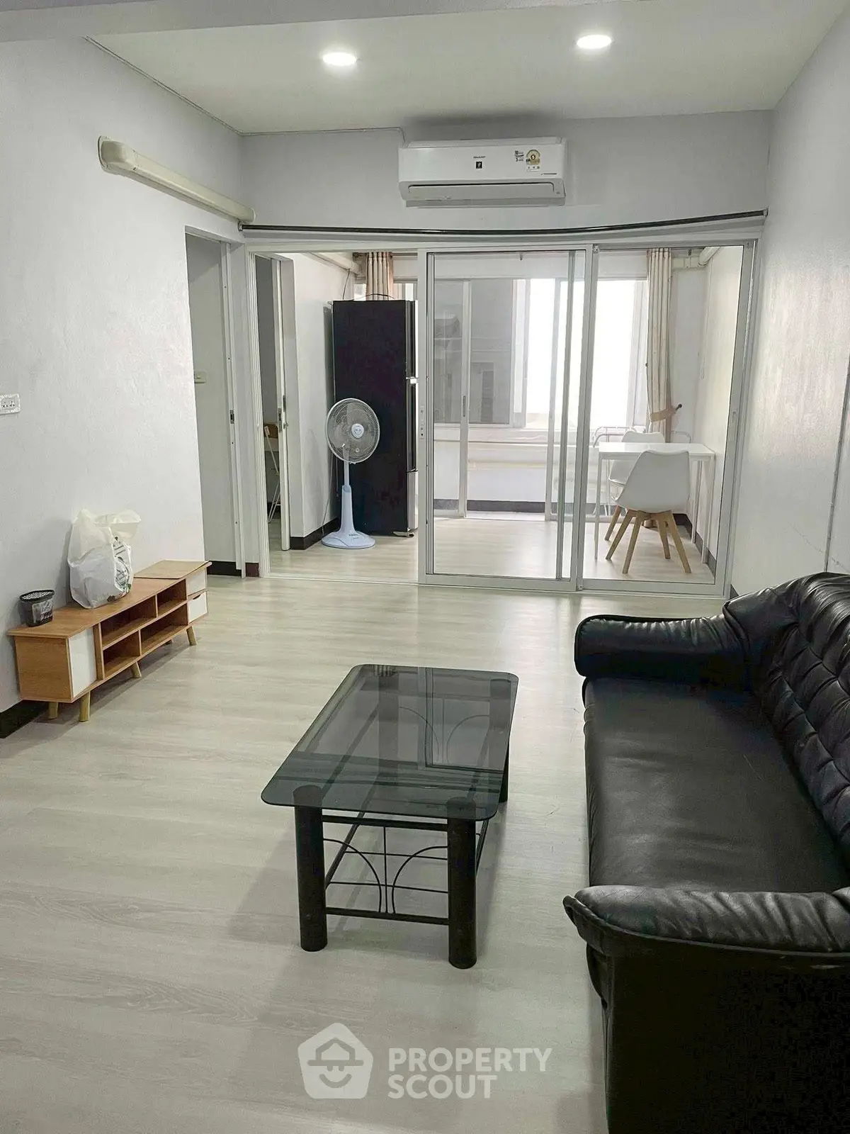 Spacious living room with modern furnishings and glass partition leading to a bright study area.