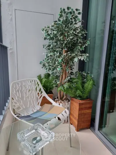 Chic balcony with modern chair, glass table, and lush greenery for a serene urban retreat.
