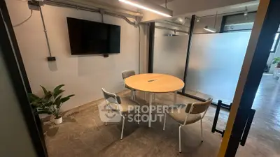 Modern office space with round table, chairs, and wall-mounted TV, ideal for meetings.