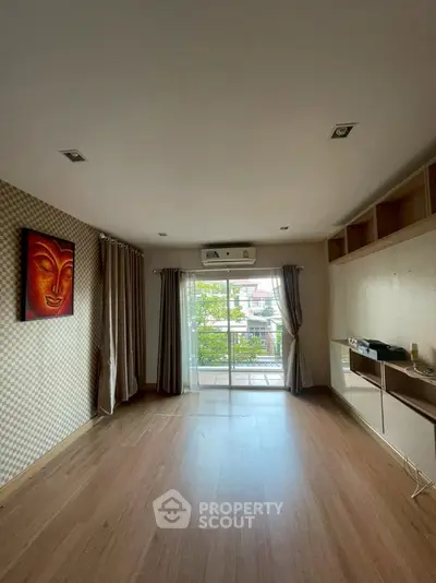 Spacious living room with wooden flooring and balcony access, featuring modern decor and ample natural light.