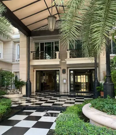 Luxurious building entrance with elegant black and white checkered flooring and lush greenery.
