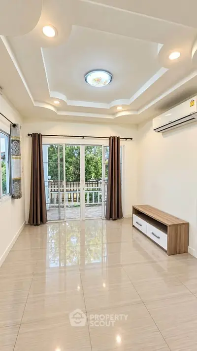 Spacious living room with modern ceiling design and large windows opening to a balcony.