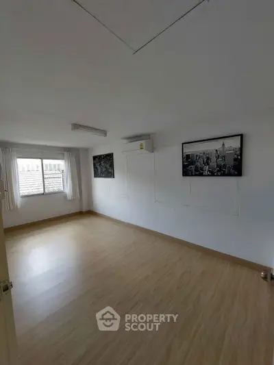 Spacious empty room with wooden flooring and air conditioning unit.