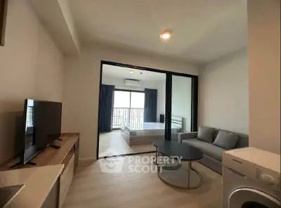 Modern living room with TV, sofa, and washing machine, leading to a bedroom with balcony view.