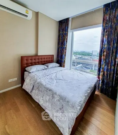 Modern bedroom with large window offering city view, featuring elegant bed and wooden flooring.