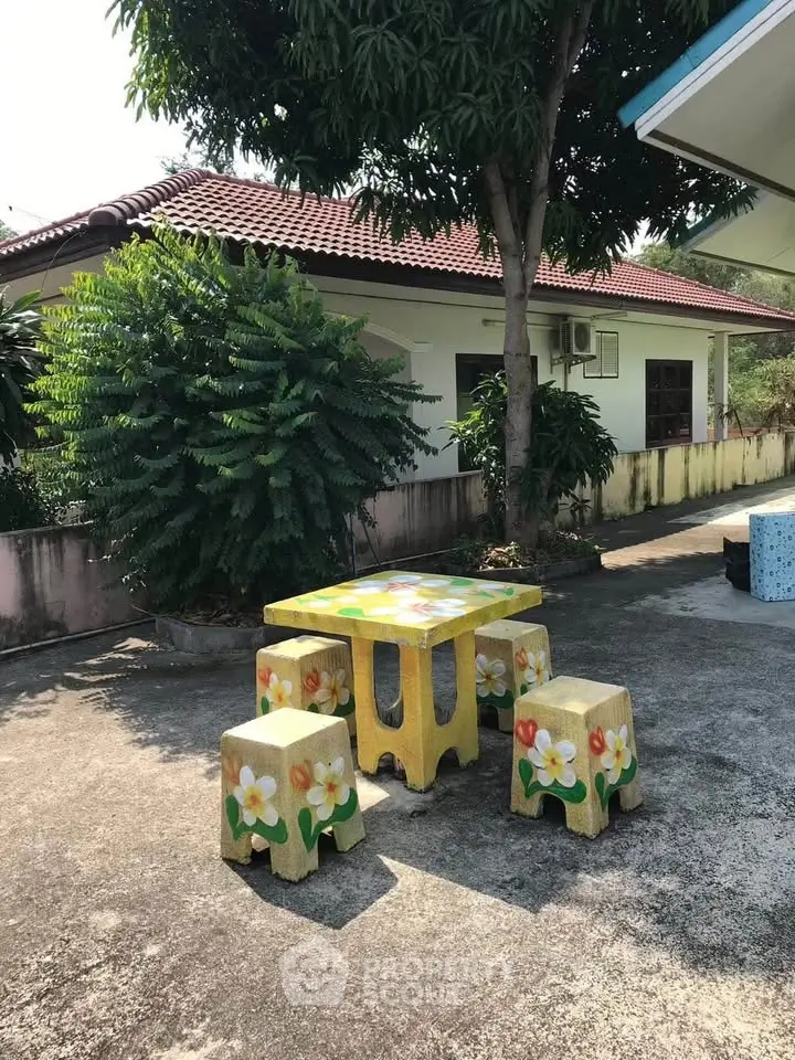 Charming outdoor patio with floral furniture set under a lush tree, perfect for relaxation.