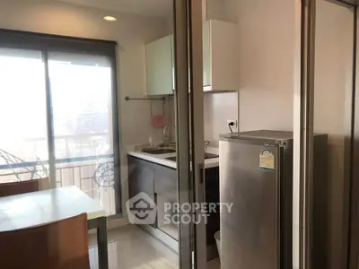 Modern kitchen with sleek cabinets and stainless steel fridge, featuring a dining area and balcony view.