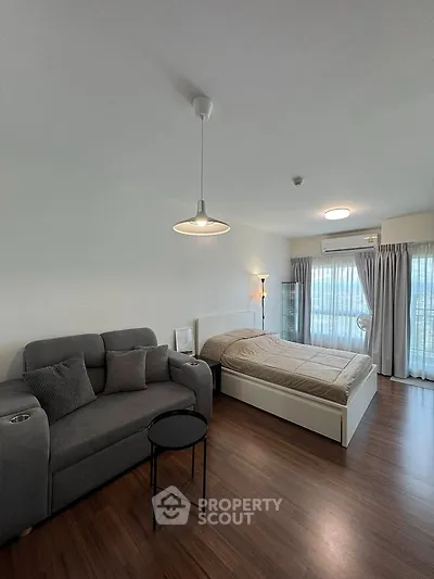 Modern studio apartment with cozy bed and stylish sofa, featuring large windows and elegant lighting.
