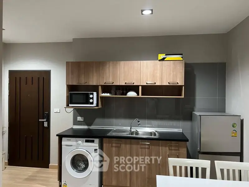 Modern kitchen with wooden cabinets, washing machine, and compact fridge in cozy apartment.