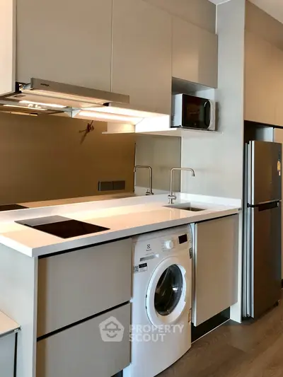 Modern kitchen with sleek appliances and integrated washing machine in stylish apartment.