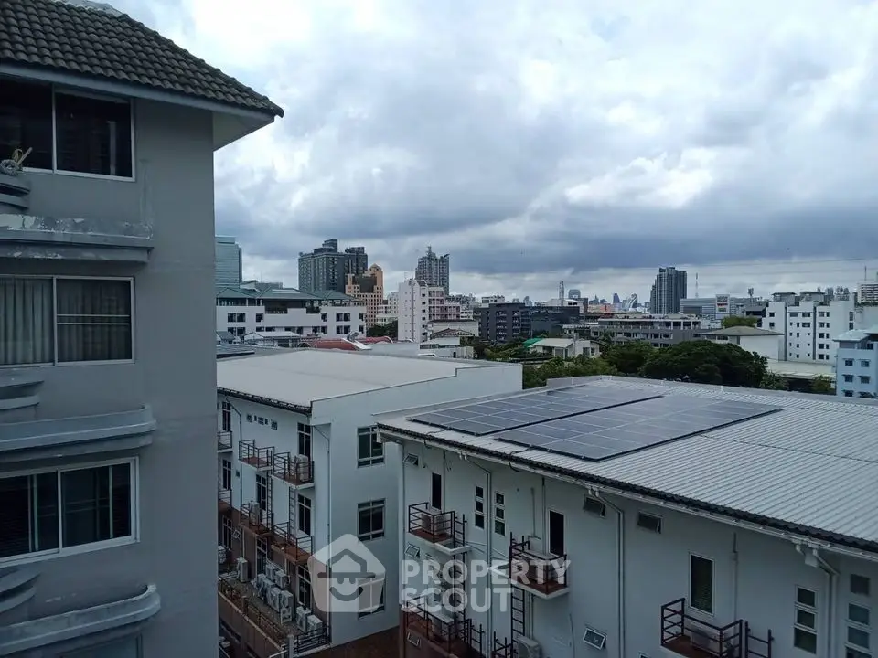 Cityscape view from apartment balcony with solar panels and cloudy sky