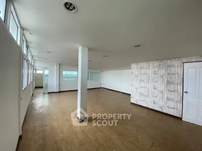 Spacious open-plan room with wooden flooring and ample natural light, ideal for versatile living or office space.