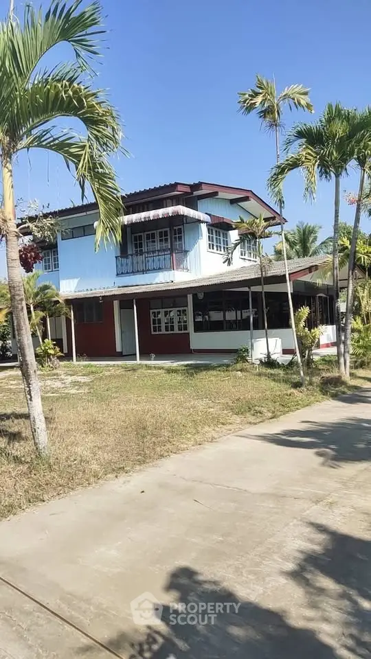 Charming two-story house with lush palm trees and spacious yard under clear blue sky.