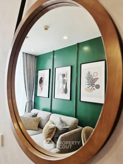 Stylish living room with green accent wall and modern art reflected in round mirror.