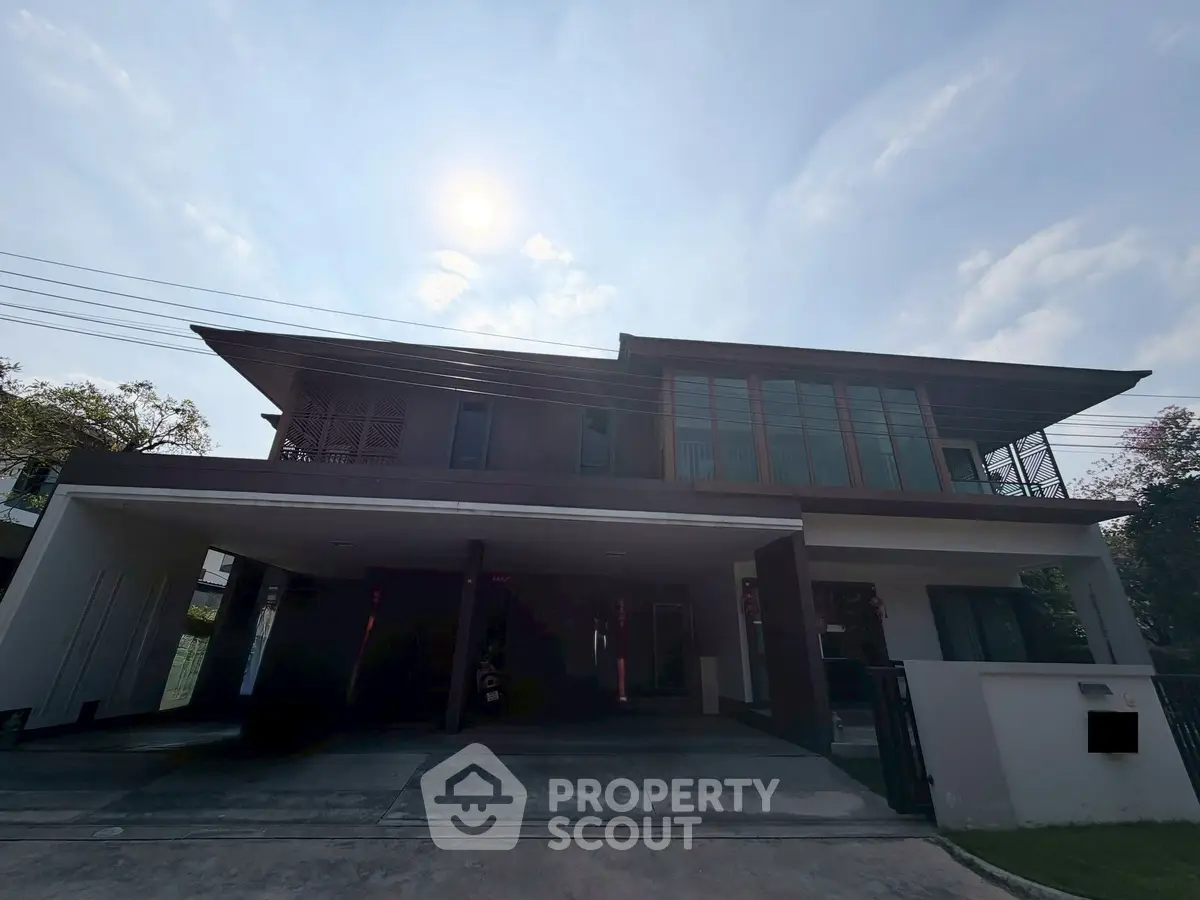 Modern two-story house with large windows and spacious driveway under a bright sky.
