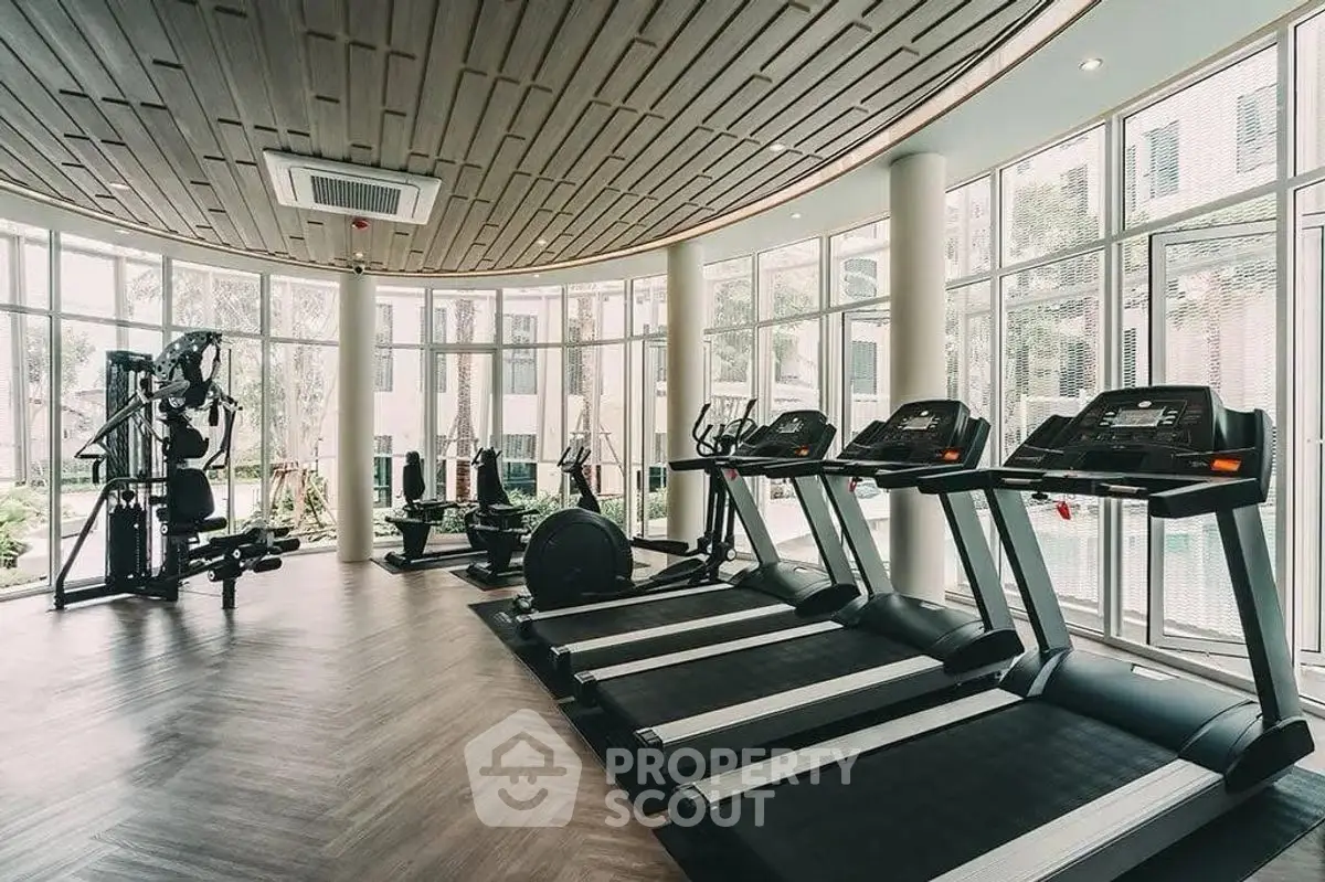 Luxurious gym with modern equipment and floor-to-ceiling windows in upscale residential building.