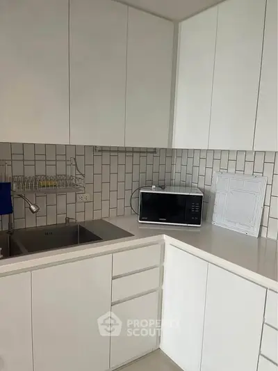 Modern kitchen with sleek white cabinets and microwave, featuring a minimalist design.