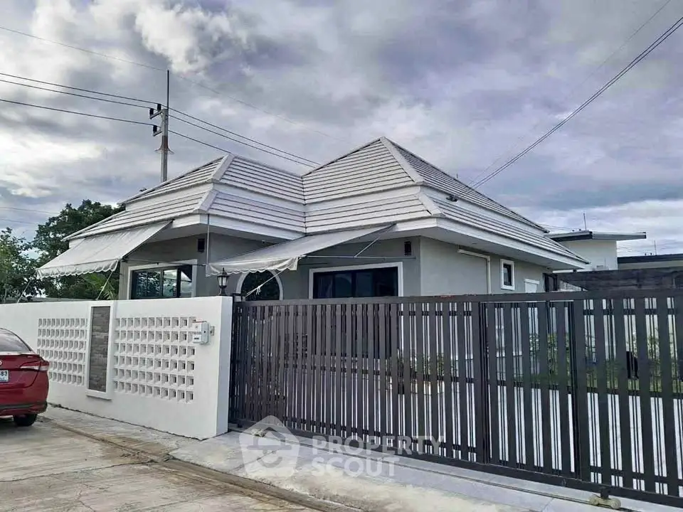 Modern single-story house with sleek design and gated entrance under cloudy sky.