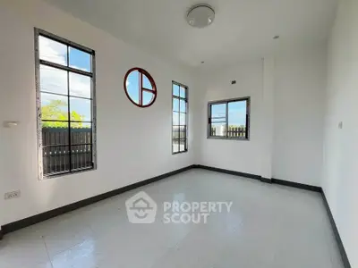 Bright empty room with unique circular window and tiled floor, ready for customization.