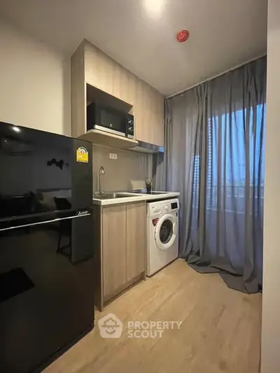 Modern compact kitchen with washing machine and microwave, featuring sleek cabinetry and large window with curtains.