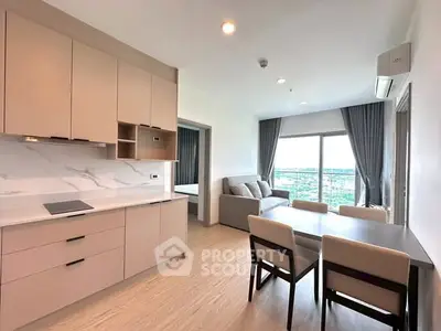 Modern open-plan living room with kitchen and dining area, featuring sleek cabinetry and large windows with a view.