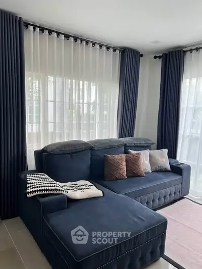 Elegant living room with plush navy sofa and floor-to-ceiling windows with sheer curtains.
