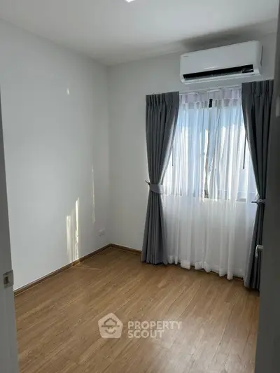 Bright empty room with wooden flooring and air conditioning, ideal for a cozy bedroom setup.