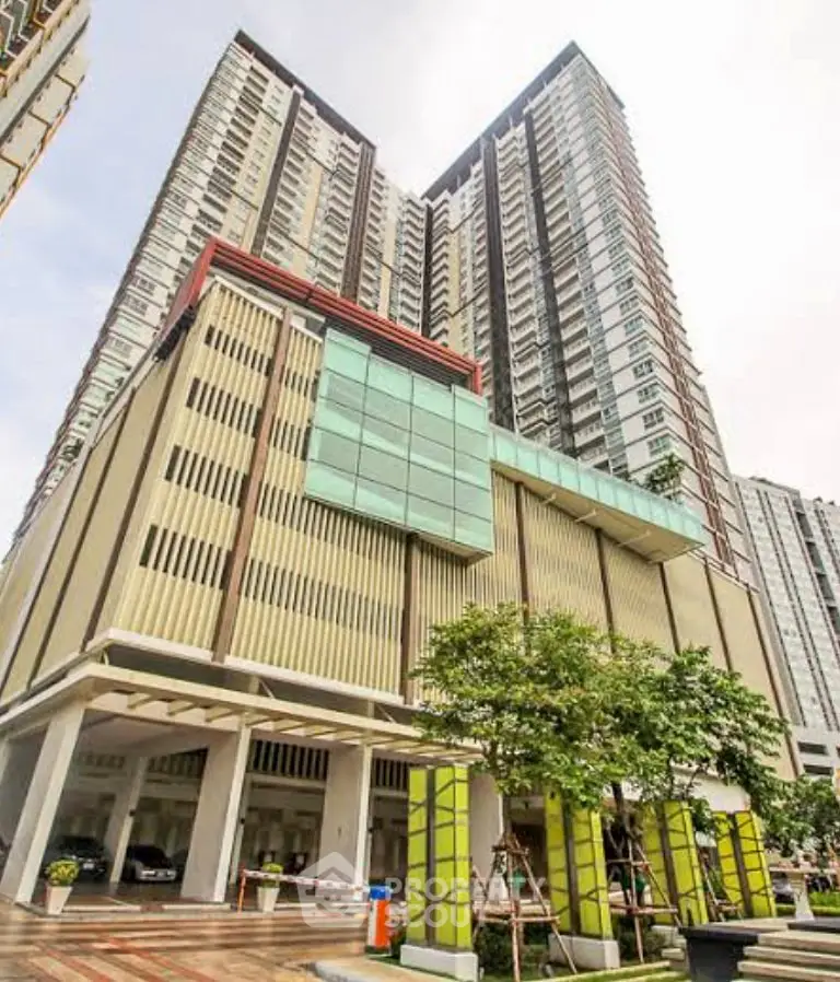 Modern high-rise building with sleek architecture and lush greenery at the entrance.