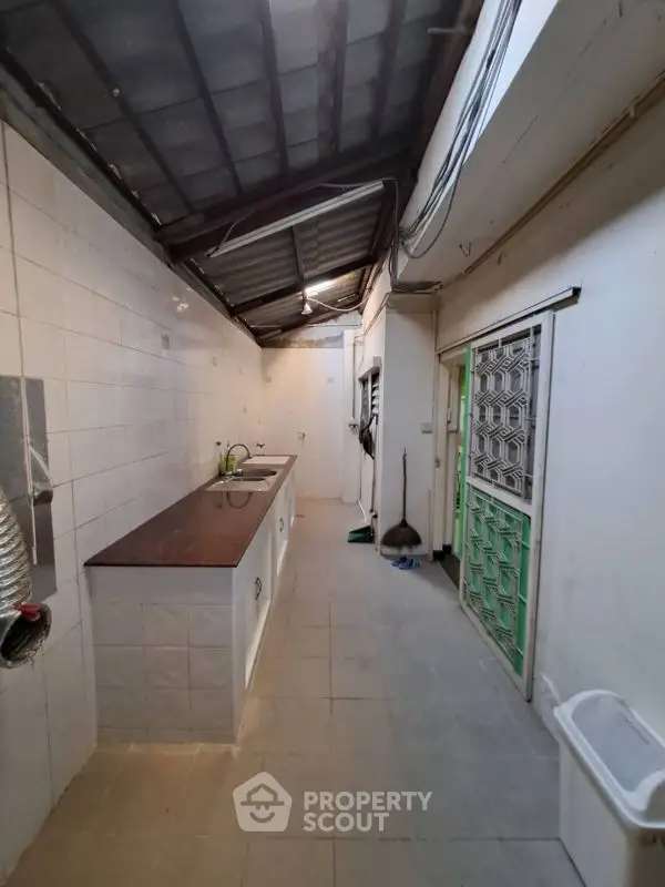 Spacious kitchen with tiled walls and countertops, featuring a double sink and ample storage space.